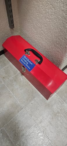 Customer's red storage case labeled with a sticker for the NovaCare One-Button Anti-Choking Device sitting on a floor.