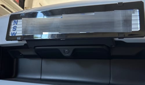 Customer's black Porsche 911 miniature plinth mounted on the car's front bumper, perfectly aligned with the bumper components.