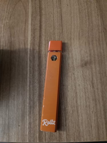 Customer's orange Rollz THCA vape pen laying flat on a wooden surface.
