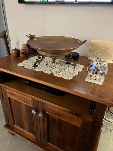 Customer's metallic decorative bowl placed on a doily atop a wooden media console.