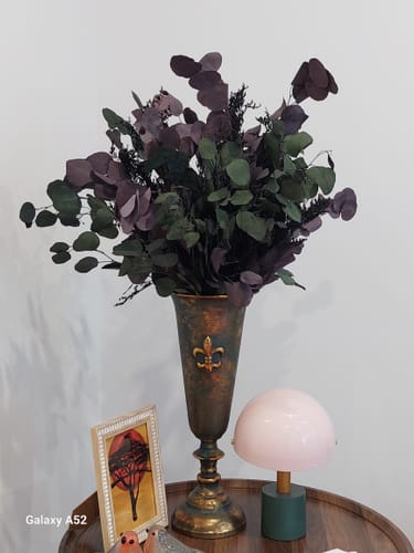 Customer's Guido French Provincial urn vase filled with dried dark foliage, sitting on a round wooden table.