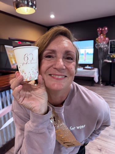 Reviewer holding a 60th birthday cup, smiling to show smooth skin after using The Micro Infusion System.