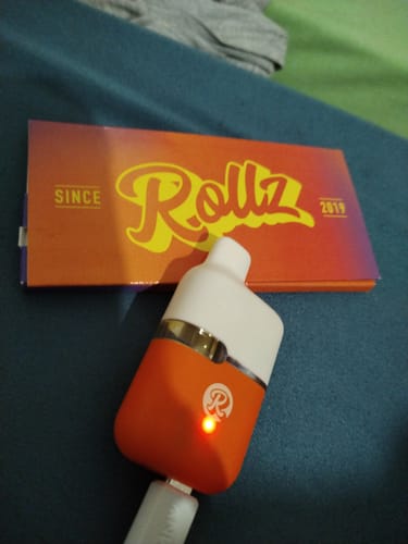 Customer's orange and white THC-A Vape charging with a glowing light, placed in front of its branded packaging.