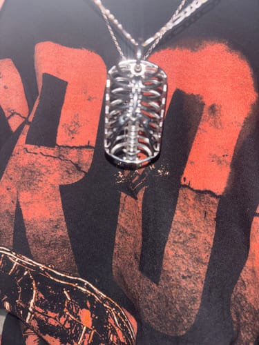 Customer's silver Ribcage Dog Tag Necklace pendant, worn around the neck against a dark graphic shirt.
