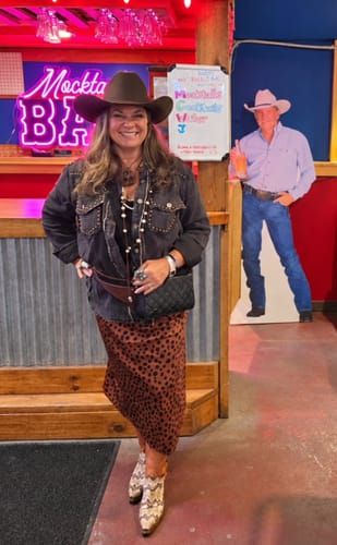 Customer's charcoal long sleeve button down top with studding details, worn with a brown skirt and cowboy hat.