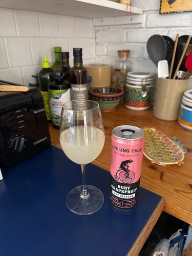 Customer's Ruby Grapefruit THC Seltzer in a pink can next to a glass of pale yellow seltzer on a kitchen counter.
