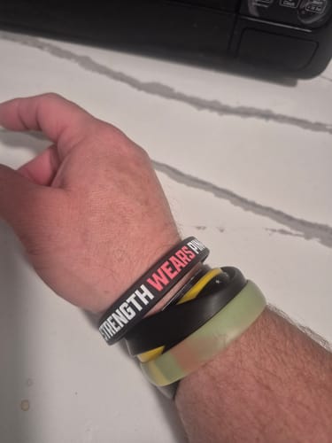 Customer's wrist wearing black Breast Cancer Awareness silicone bracelets with white and pink embossed text.