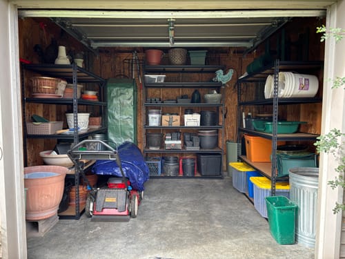 Customer's black metal garage shelving units filled with various storage bins and garden equipment in a garage.