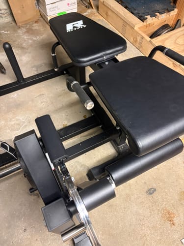 Customer's RitFit leg extension machine in a home gym, showing the black padded seat and adjustable leg rollers.