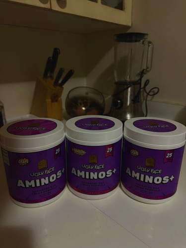 Customer's three purple tubs of UGLYFACE AMINOS+ sitting on a kitchen counter in front of a blender.