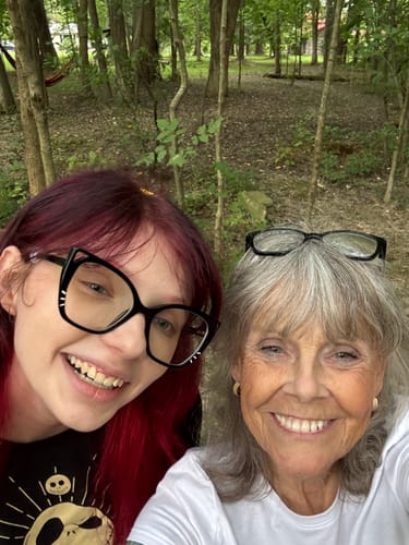 Reviewer smiling with a younger person in a natural, wooded setting.