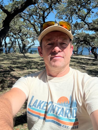 Customer's Lake Ontario Retro Stripe T-Shirt worn outdoors with trees and a lake in the background.