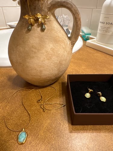 Customer's Gold Aquamarine Drop Earrings and matching jewelry set displayed on a counter with a decorative vase.