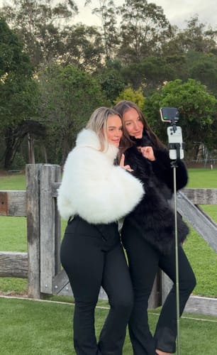 Customer's fashion ski suit with white and black faux fur jackets, being filmed outdoors by two people.
