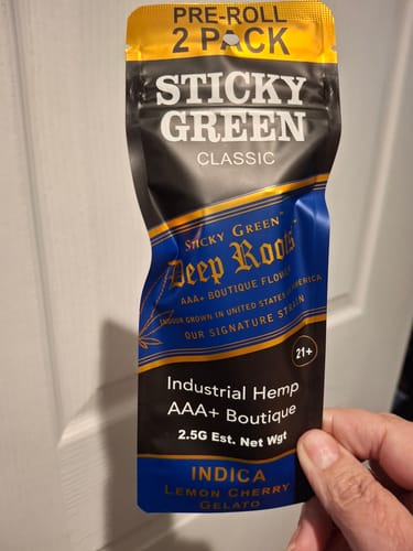 Reviewer's hand holding a sealed Sticky Green Deep Roots Lemon Cherry Gelato pre-roll packet.