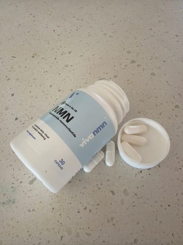 Flacon ouvert de gélules Pure NMN de la cliente, avec plusieurs pilules blanches renversées sur une surface claire et mouchetée.