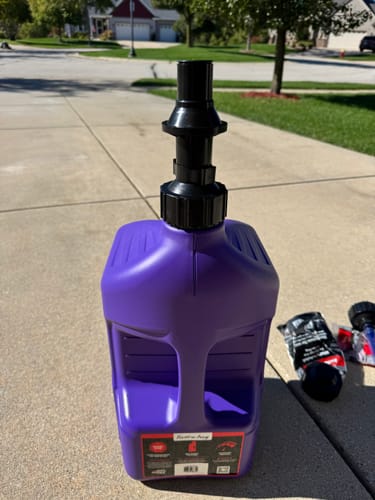 Customer's purple Tuff Jug 5 Gallon utility jug with spout attachment standing on a driveway.