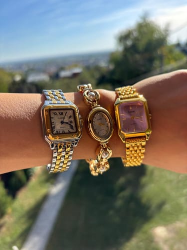 Customer's hand wearing three distinct Claire De Mains metallic watches with gold and silver details outdoors.