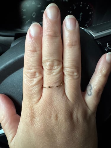 Reviewer's hand wearing an Ariel Mini Pearl gold ring on their middle finger while holding a steering wheel.