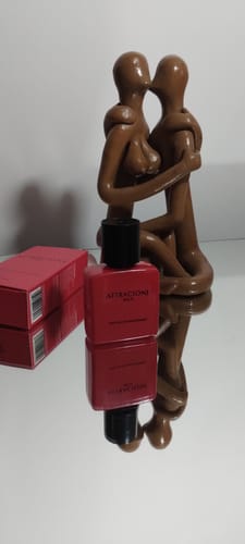 Customer's Attracione Men perfume bottle and red box placed next to a decorative brown kissing couple statue on a mirror.