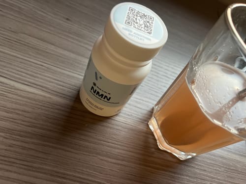 Flacon blanc Pure NMN du client à côté d'un verre de liquide sur une surface en bois.