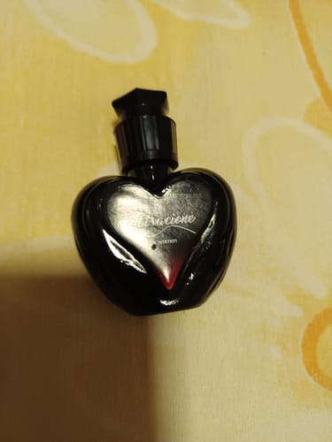 Customer's Attracione Sensual perfume, a small heart-shaped black bottle resting on a yellow surface.