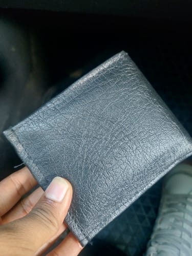 Customer's black faux-leather wallet, showing the plain exterior surface held in hand.