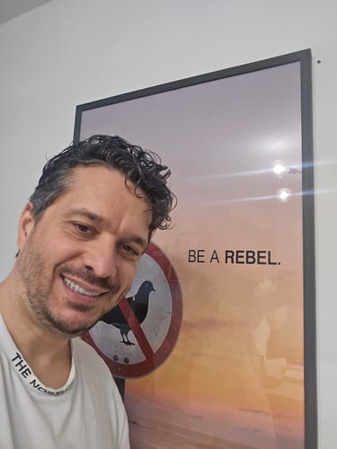 Customer smiling next to their framed Be a Rebel wall art print featuring a bird on a red sign.