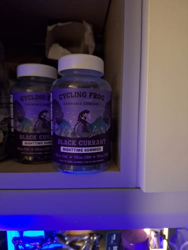 Customer's two bottles of Cycling Frog Black Currant Nighttime Gummies resting on a shelf in a dark room.