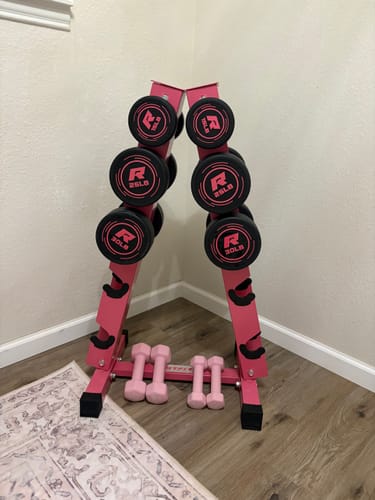 Reviewer's RitFit pink PVC-coated round dumbbells on a pink A-frame stand in a corner.