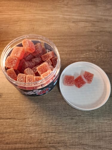 Customer's THC Space Cubes Gummies in an open jar with three cubes placed on the white lid on a wooden table