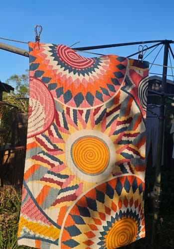 Customer's Student Cotton Gauze Pillow Towel with vibrant sun and spiral patterns, hanging outdoors on a clothesline.