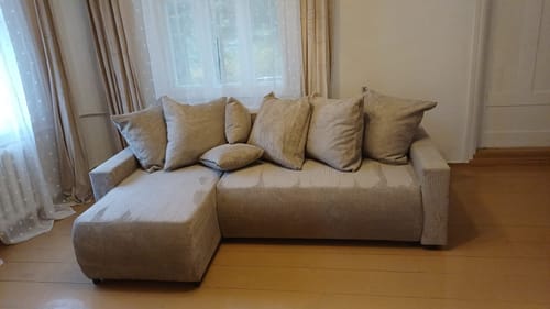 Reviewer's šviesus POLO minkštas kampas su pagalvėmis, pastatytas kambaryje prie lango.