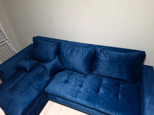 Kliento LOKO kampinė sofa tamsiai mėlynos spalvos aksominiu paviršiumi, pastatyta kambaryje.