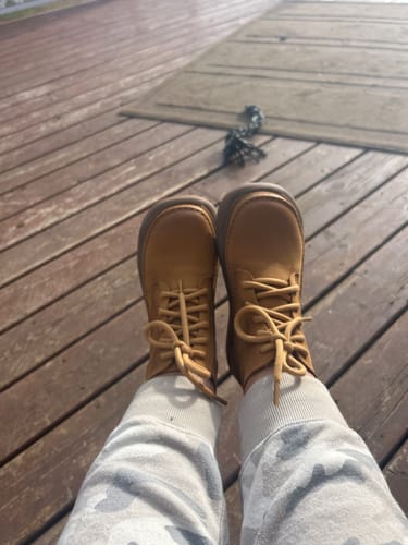 Customer's yellow genuine leather boots on feet, worn outdoors on a wooden deck.