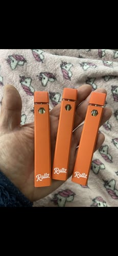 Customer's hand holding three orange Rollz THCA vapes, each branded with a logo.