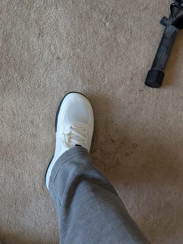Customer's white CUURT Muuv wide toe box court shoe on a carpeted floor.