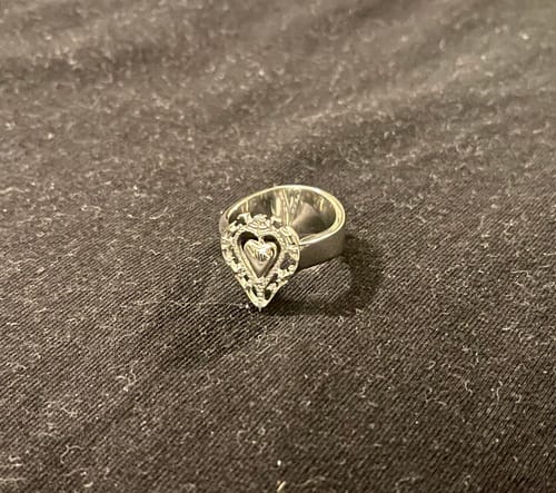 Customer's Antique Heart Ring, a silver-toned metal ring with a detailed heart design, resting on a textured fabric.