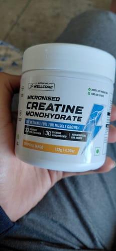 Customer's hand holding a white, round Wellcore Creatine Monohydrate container with Tropical Tango label