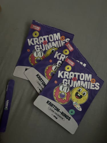 Reviewer's drei Packungen Kratom Gummibärchen auf einer grauen Oberfläche