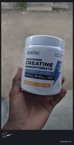 Customer's hand holding a white tub of Wellcore Pure Micronised Creatine Monohydrate Tropical Tango powder.