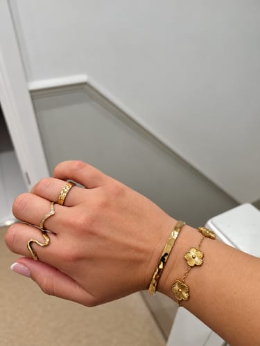 Customer's hand wearing a gold Dorcas Hammered Ring alongside other gold-toned rings and a clover-style bracelet.