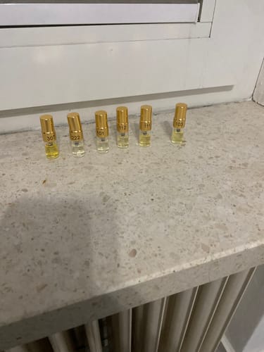 Customer's Tester Set featuring six small, glass perfume vials with gold caps arranged on a light stone windowsill.