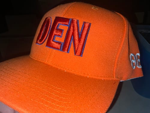 Customer's orange Custom Baseball Cap with red embroidered DEN letters and white side text, close-up.