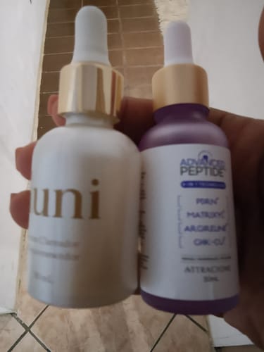 Reviewer's hand holding a bottle of Advanced Peptide serum next to another skincare bottle.