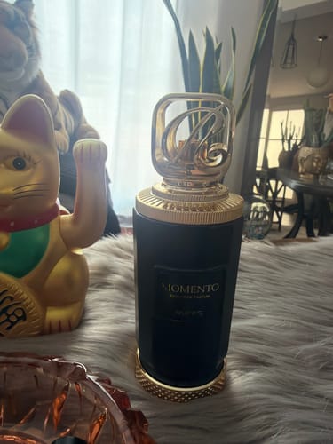 Customer's Perfume Riiffs Momento in a black cylindrical bottle with gold lid on a fur surface next to a lucky cat.