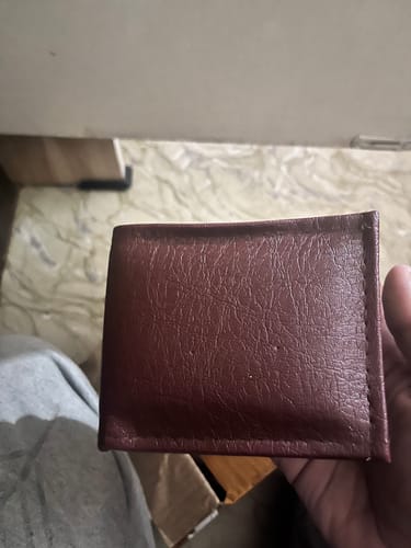 Customer's hand holding a brown textured bifold wallet, which differs from the advertised Spiderman design.