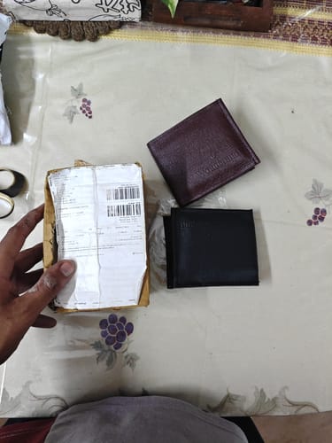 Customer's shipping package next to two leather wallets on a table, one brown and one black.