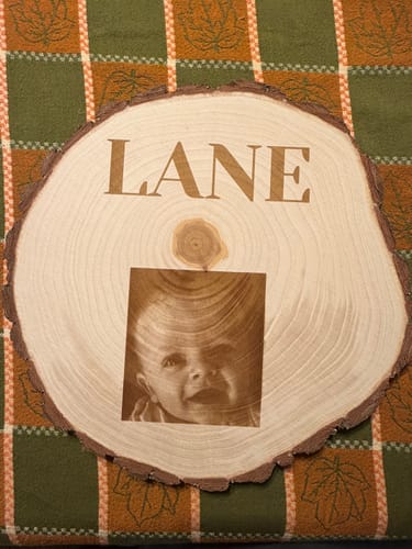 Customer's AtomStack Swift laser engraving on a round wood slice showing the name Lane and a portrait.