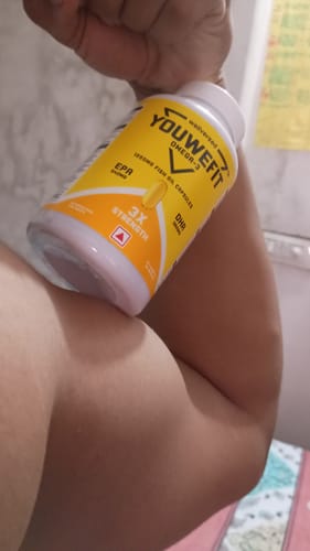 Reviewer's arm muscles flexed while holding a bottle of YouWeFit Omega-3 Fish Oil.